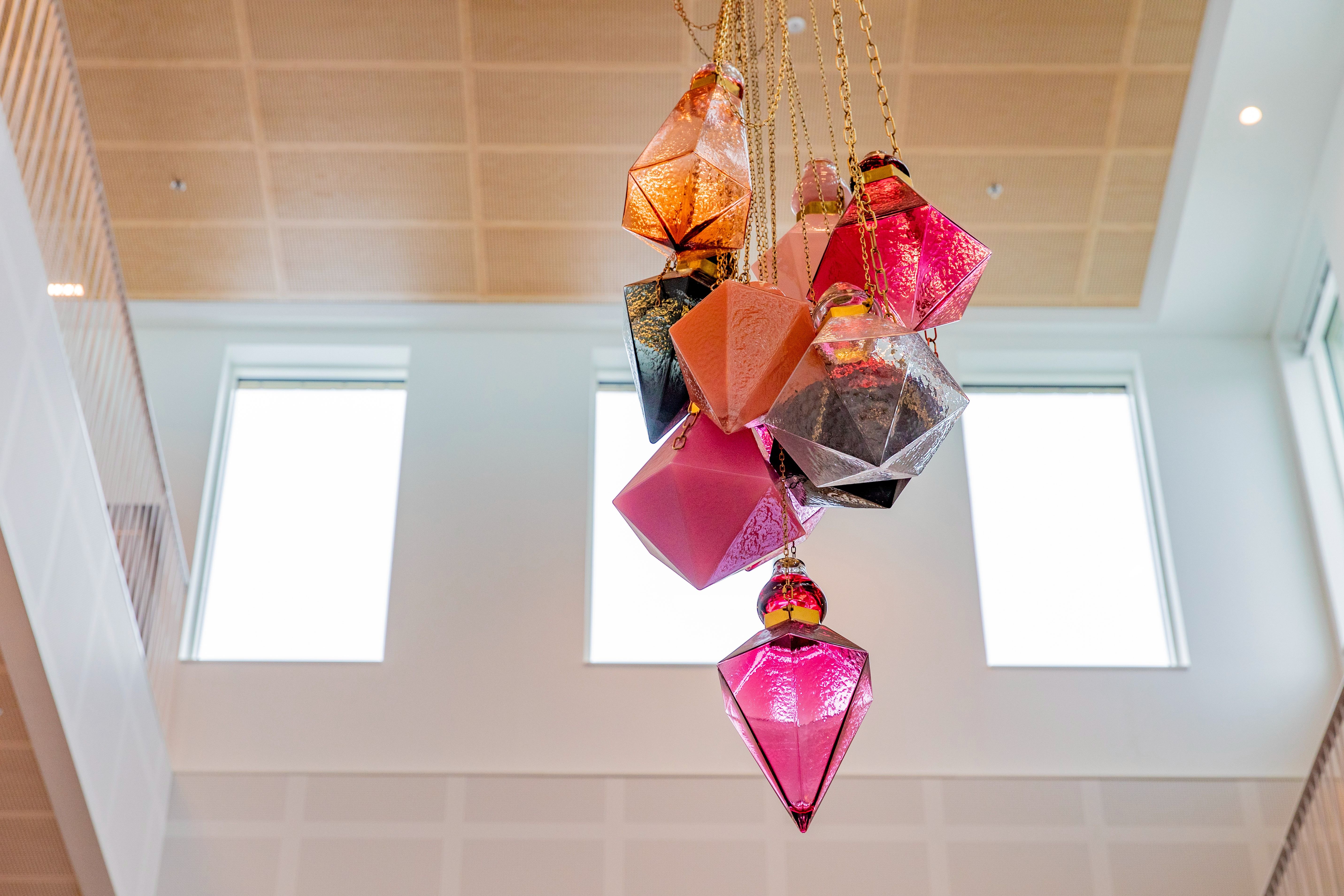 Glaskonstverk i olika rosa, oranga och svarta färger hänger i taket