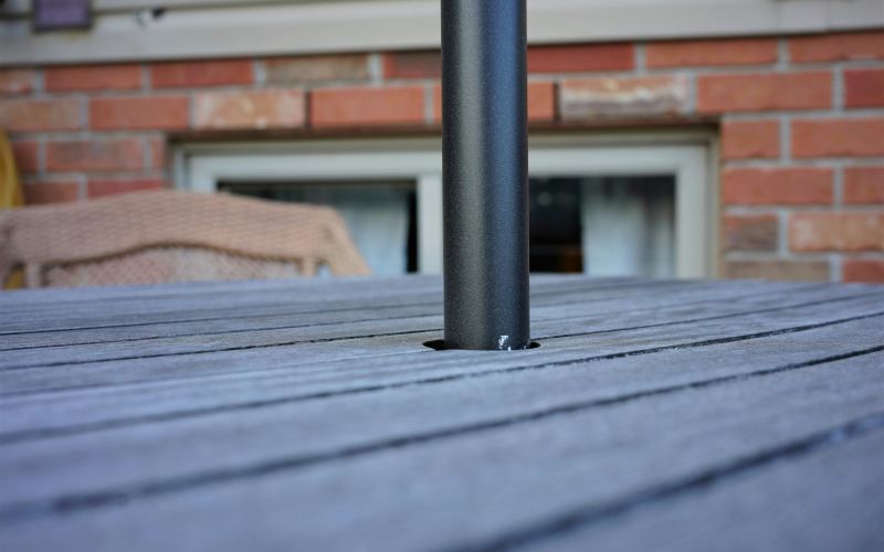 Del av träbord och stol och del av solparasoll som sticker ut ur ett hål.