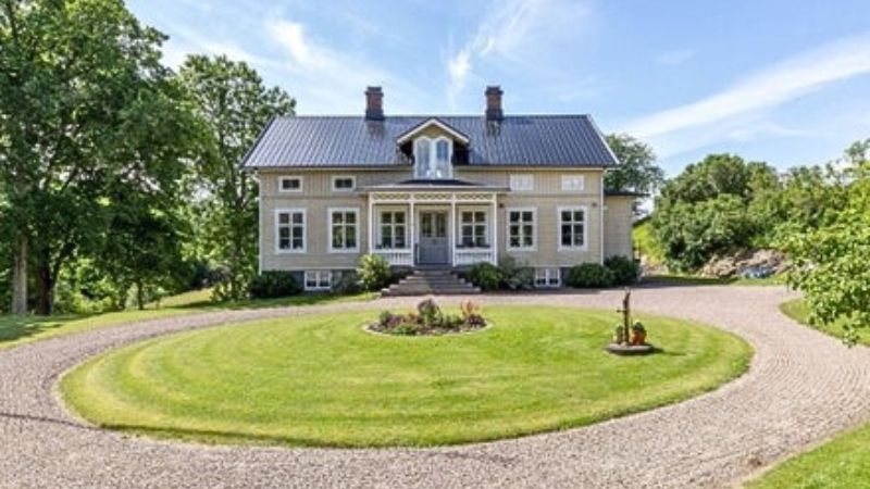 Lantligt hus i beige grå ton bakom en grön rundel.
