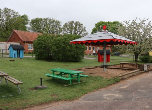 Bord, bänkar och sandlåda med lekhus i bakgrunden