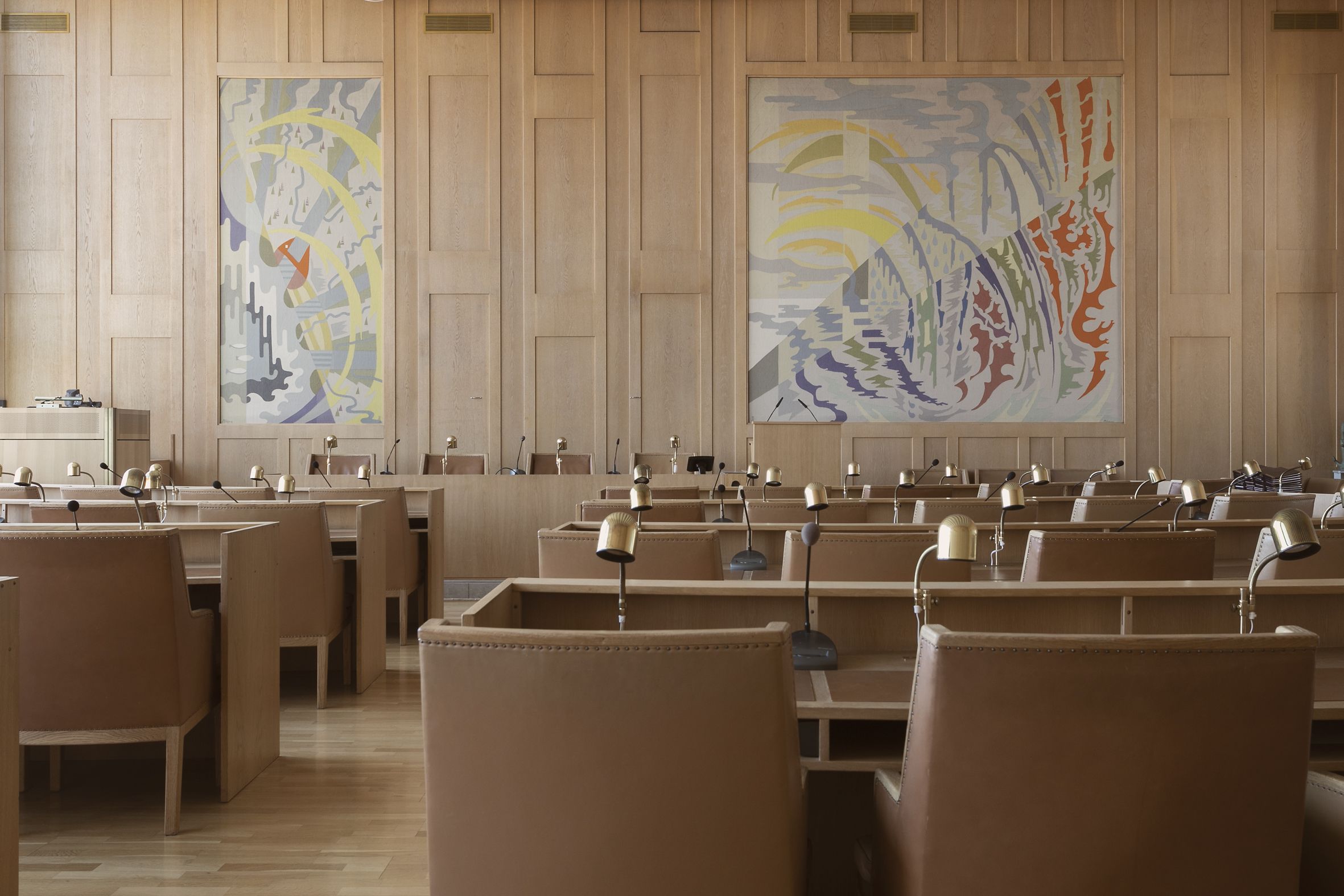 Kommunfullmäktigesalen. Stolar, lampor och tavlor i textil syns.