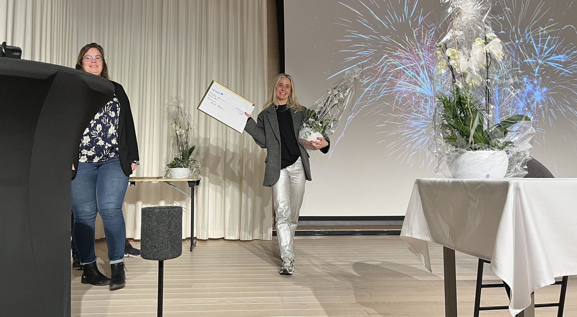 Sara Claesson går mot kameran med blomma, check och diplom i handen.