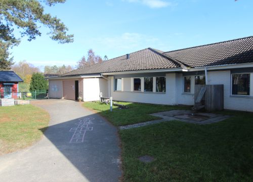 Asfaltsgång med målad hage, gräs på båda sidor och låg vit byggnad