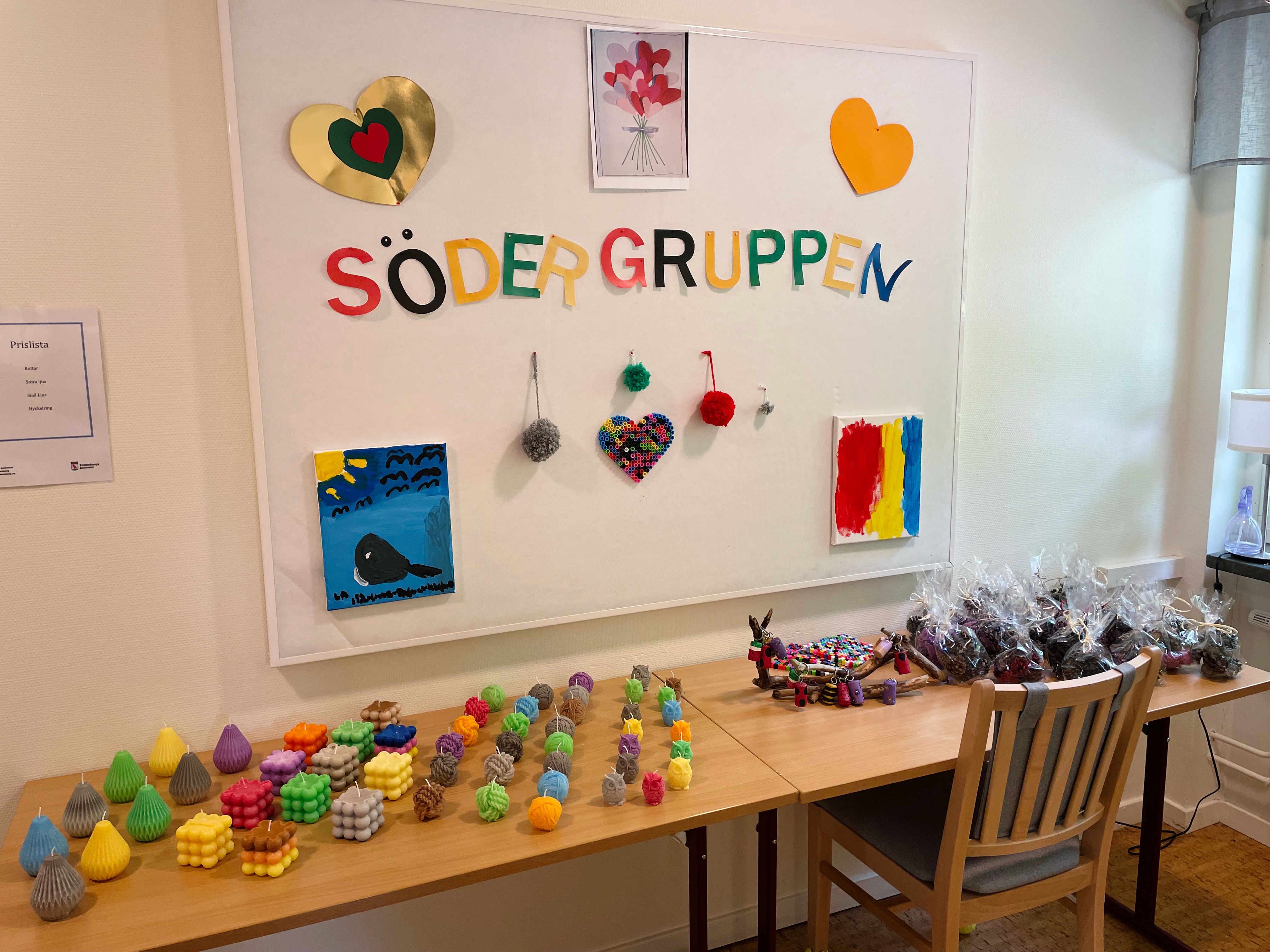 Ljus på ett bord. På väggen ovanför bordet hänger det en vit tavla där det står Södergruppen.