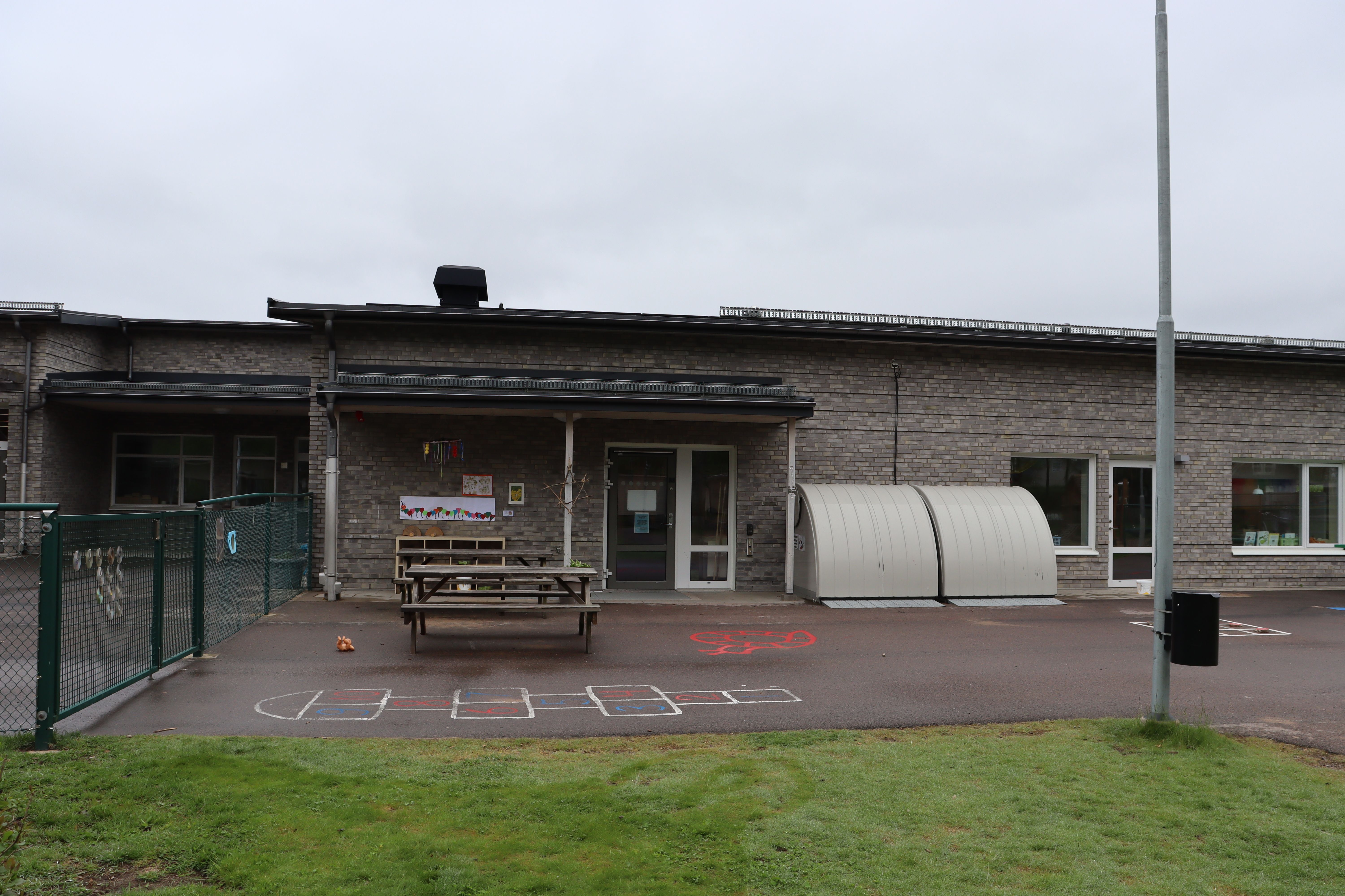 Låg grå byggnad med ritad hage på marken framför