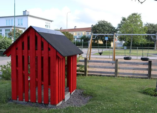Röd lekstuga - gungor i bakgrunden