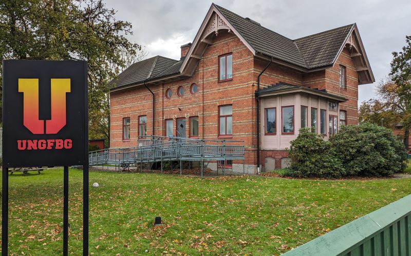 Skylt med texten Ung Fbg och i bakgrunden en röd tegelbyggnad