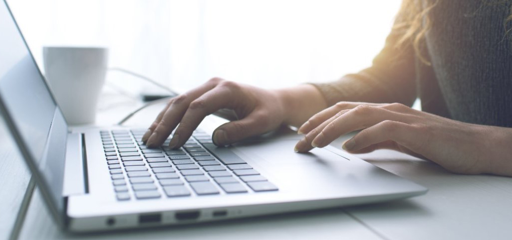 Bärbar dator på ett bord och händer som trycker på tangenterna.