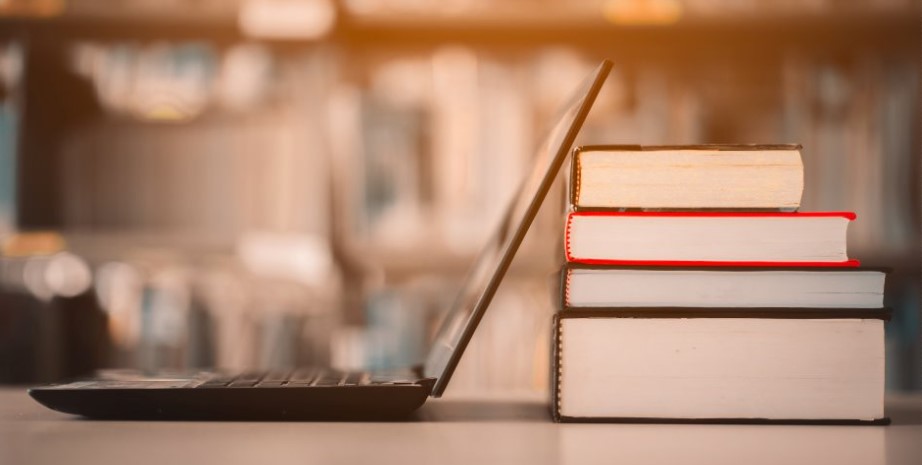 Bärbar dator på ett bord bredvid en hög med böcker.