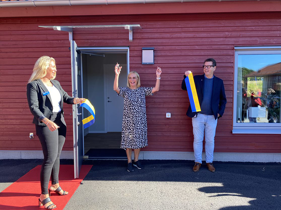 En jublande kvinna som precis har klippt av ett gult och blått invigningsband som en man och en kvinna håller. 