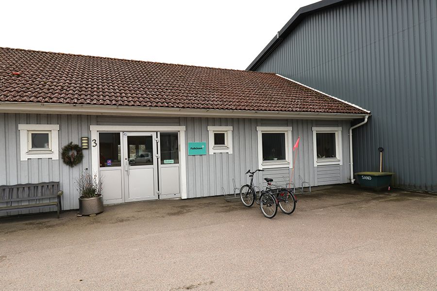 Entrén till en låg, grå träbyggnad.