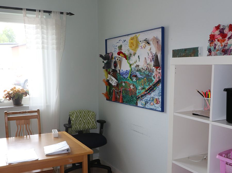 Rum med skrivbord, hylla och en färgglad tavla på väggen.