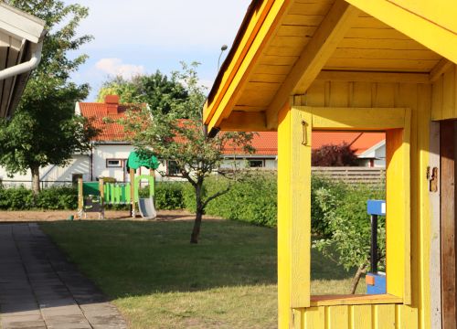 Gul lekstuga med fruktträd och klätterställning i bakgrunden