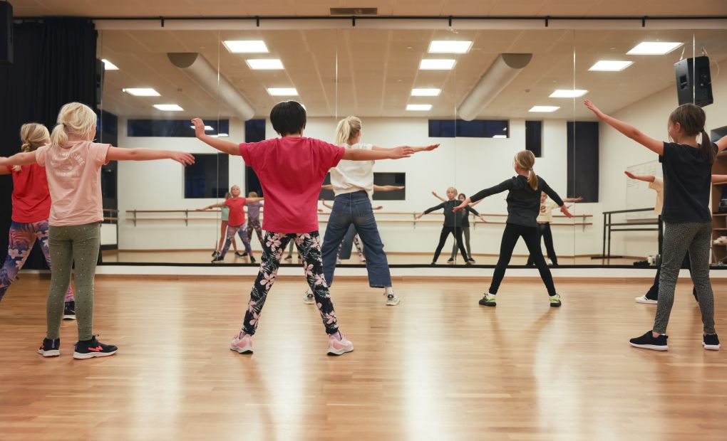 Barn som dansar framför en spegel i en danssal.