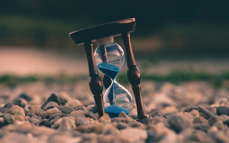 Ett timglass som lutar snett på en mark av småsten.