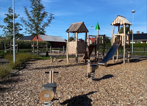 Klätterställning med rutschkana, sandlåda, träbåt och leksaker i bakgrunden