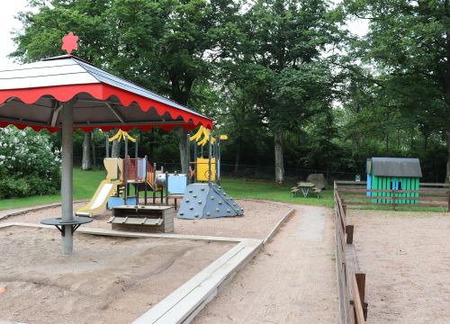 Sandlåda med solskydd, klätterställning och lekstugor i bakgrunden