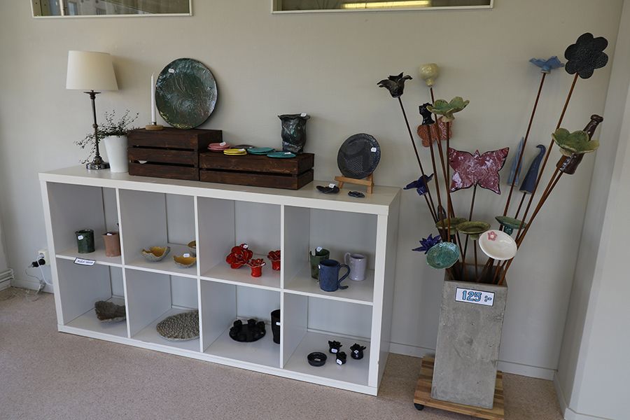 Keramikföremål står i och på en hylla. Bredvid hyllan står en hög kruka fylld med keramikföremål som satts fast på pinnar av armeringsjärn.