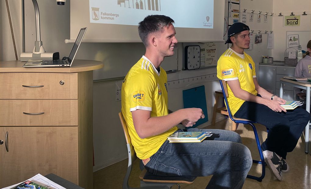 Två fortbollsspelare från Falkenbergs FF, iklädda gula lagtröjor, sitter i ett klassrum och läser.