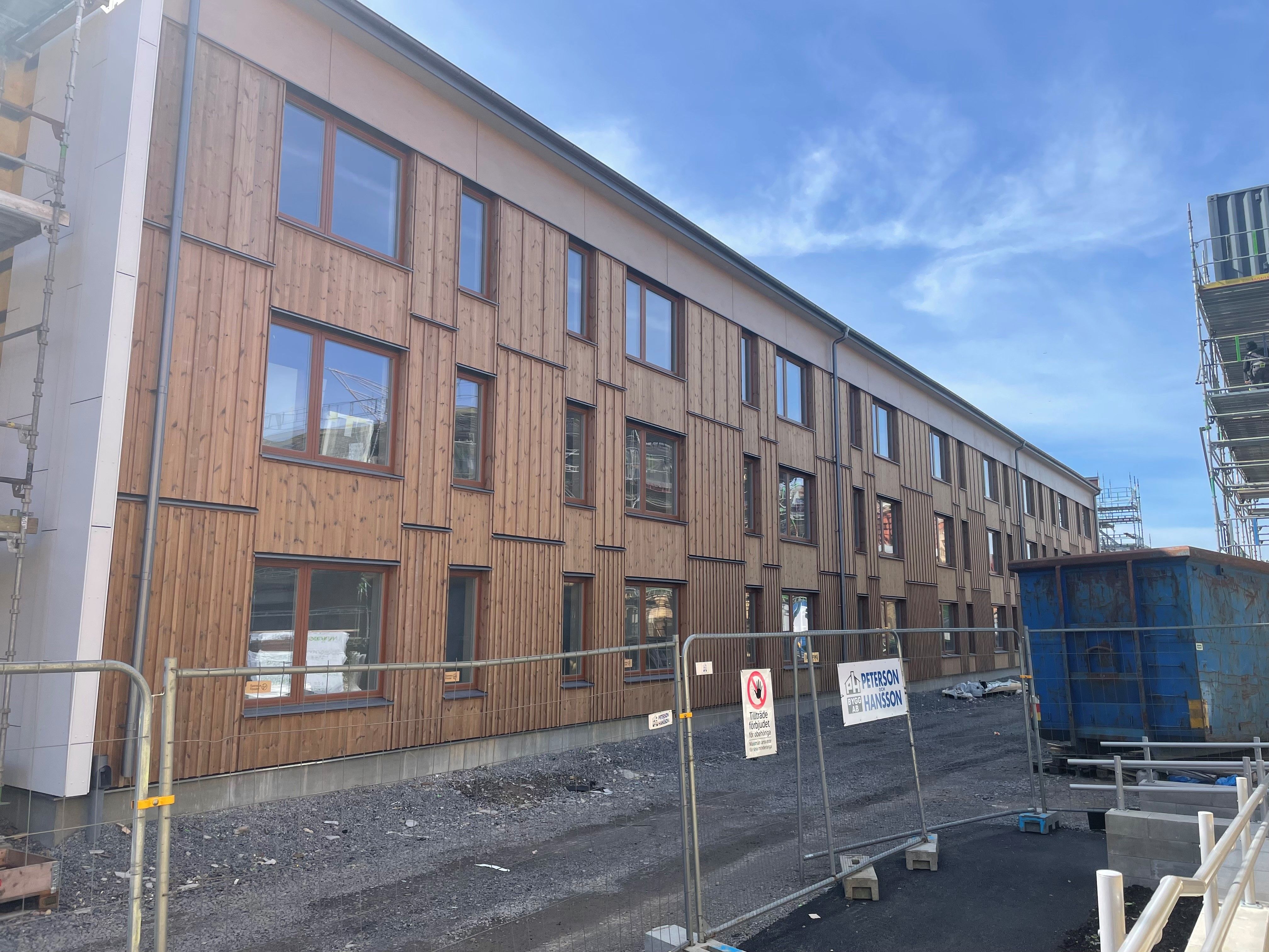 Byggnad med mörk träfasad bakom ett byggstaket.