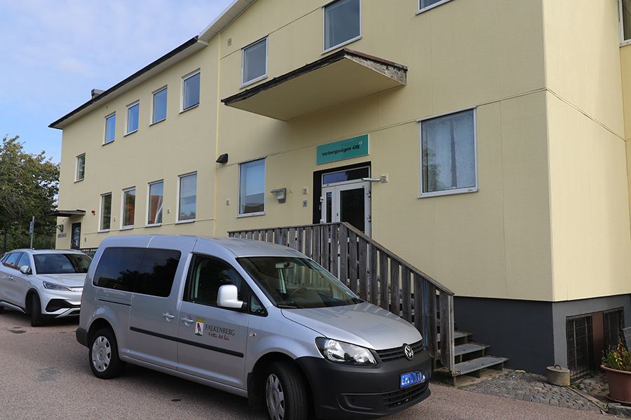 Entrén till ett gult hus. Framför huset står en grå bil med kommunens logga på.