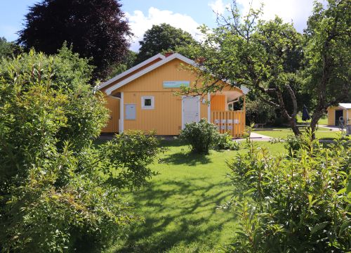 Sandlåda med gungleksak, balansbana, gräsmatta och gult hus i bakgrunden