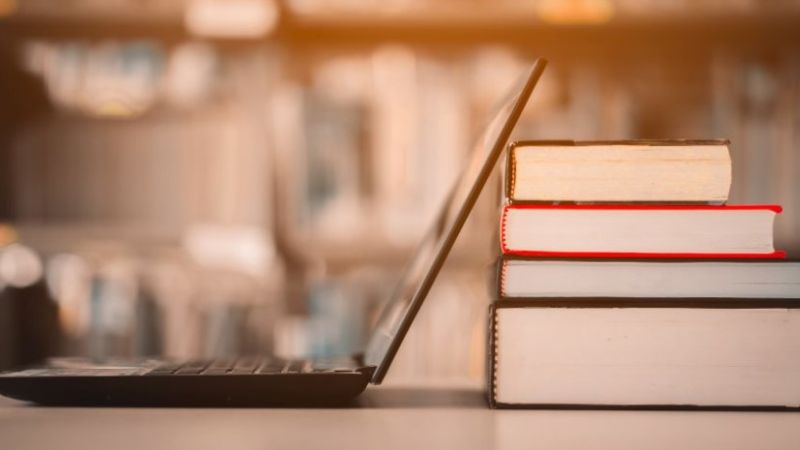 Bärbar dator på ett bord bredvid en hög med böcker.