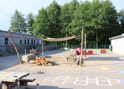Asfaltsplan med målad hage, sandlåda med solskydd och leksaker