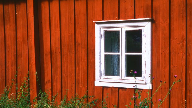 Röd träfasad och ett vitt fyrkantigt fönster.