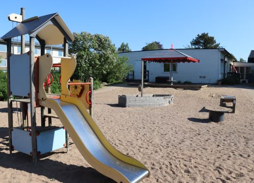 Klätterställning med rutschkana, sandlåda, träbåt och leksaker i bakgrunden