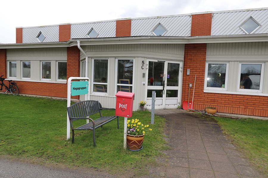 Entré till orange tegelbyggnad. Framför entrén står en svart bänk och en röd postlåda.