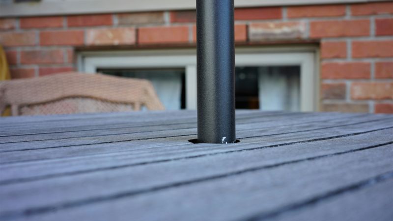 Del av träbord och stol och del av solparasoll som sticker ut ur ett hål.