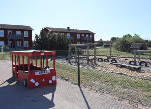 Lekbrandbil med balansbana och röda hus i bakgrunden