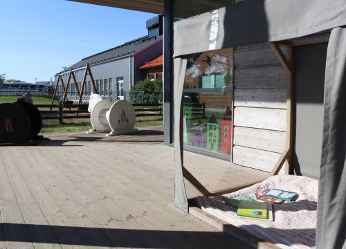 Uteläshörna med filt och böcker, trähästar i bakgrunden