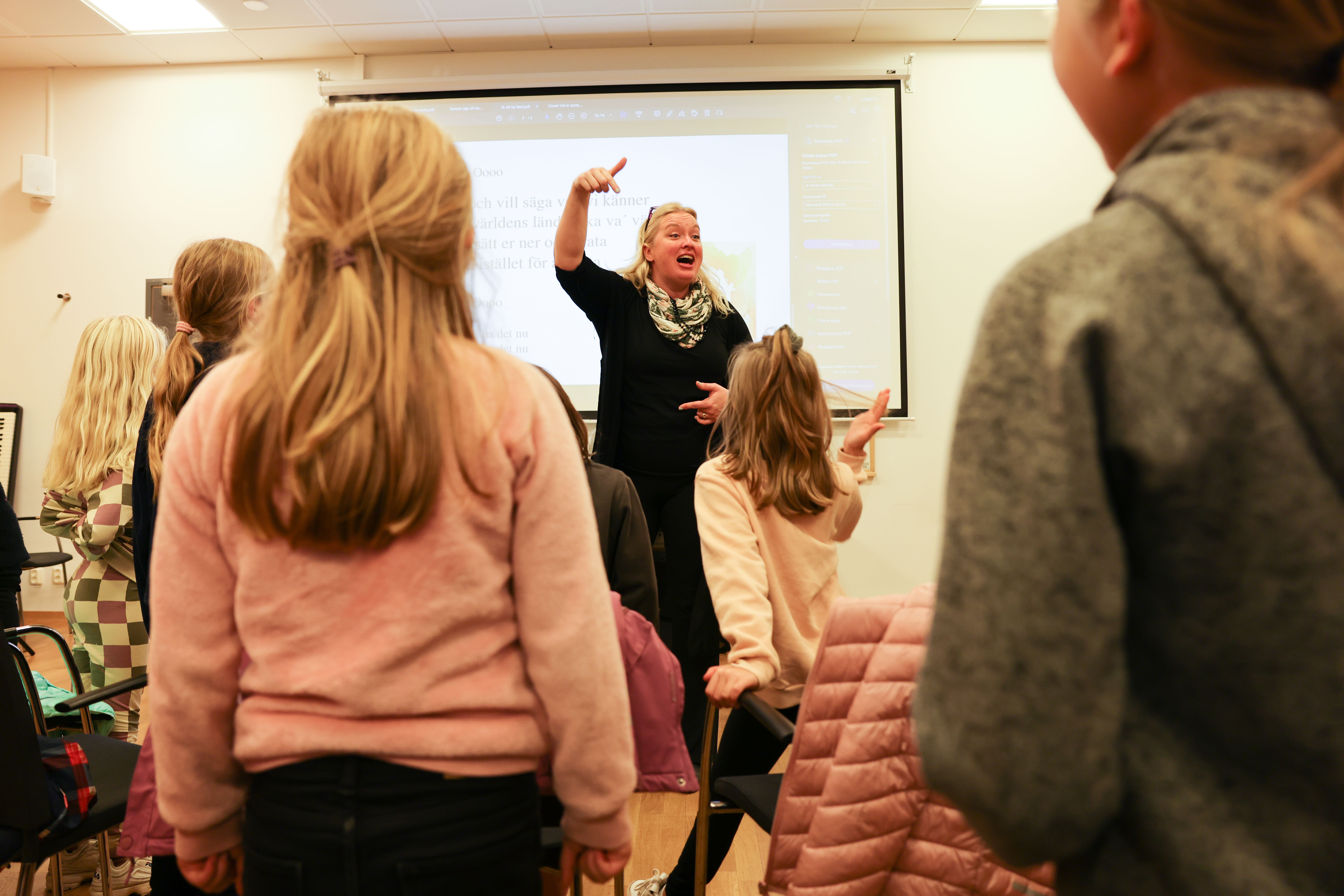 Barn på sånglektion står framför en körledare som sjunger