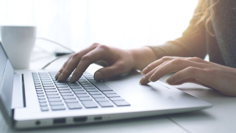 Bärbar dator på ett bord och händer som trycker på tangenterna.