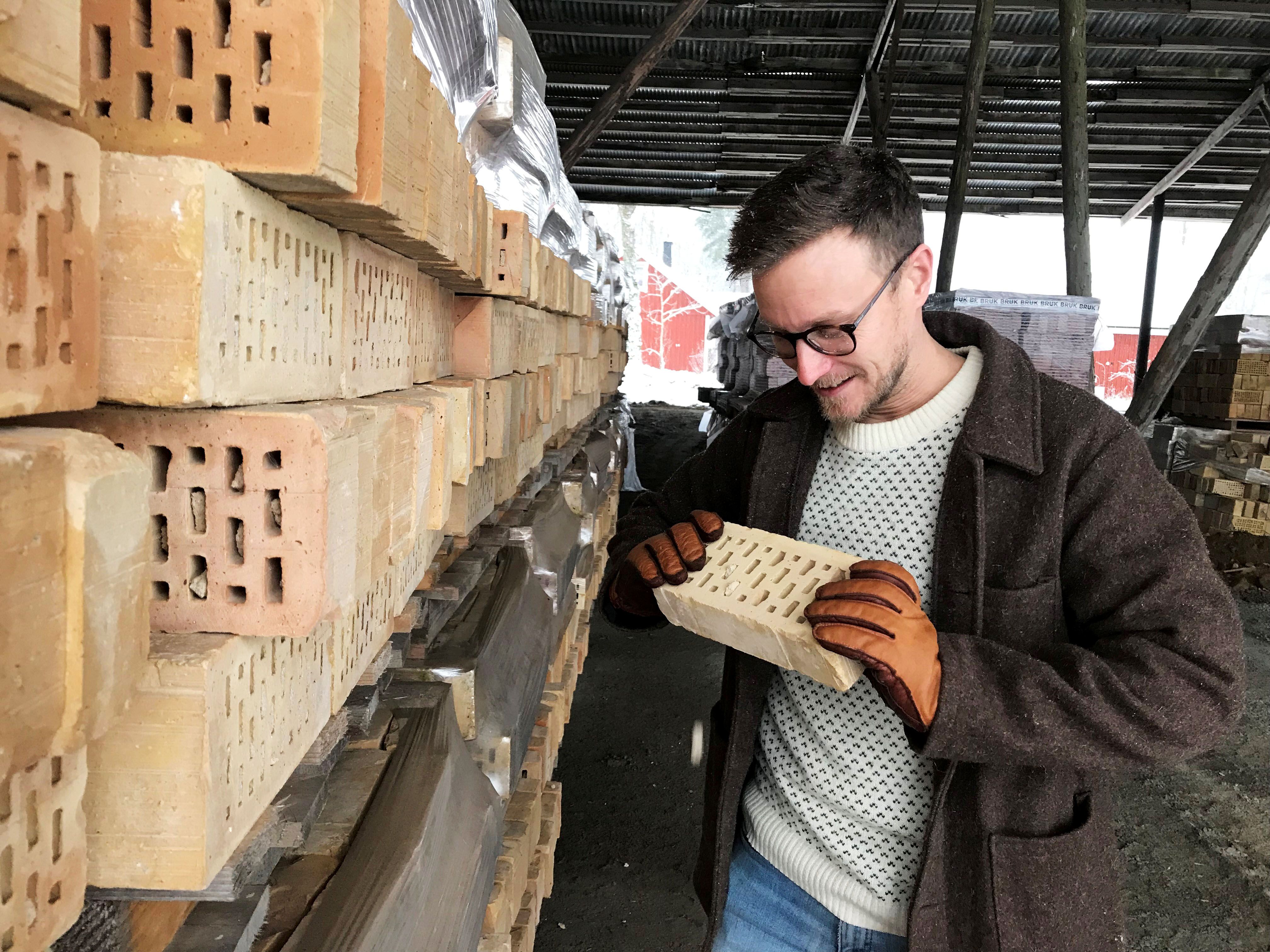Carl tittar på en ljus tegelsten utomhus vid lager av tegelstenar.