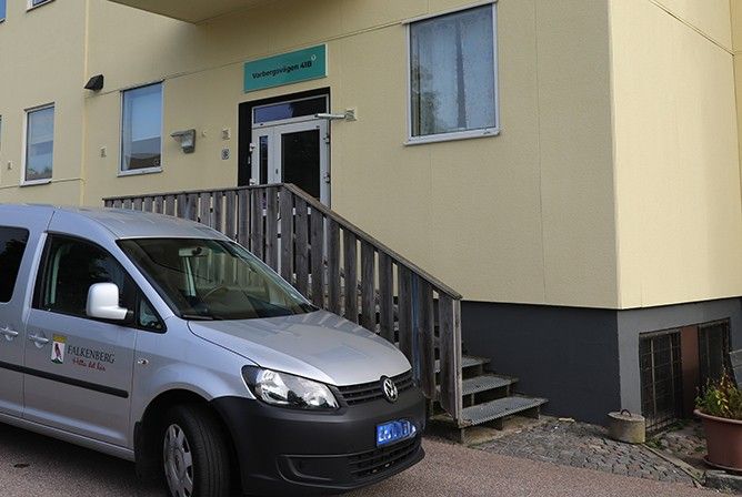 Entrén till ett gult hus. Framför huset står en grå bil med kommunens logga på.