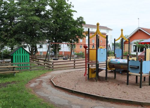 Klätterställning i sandlåda med grön lekstuga i bakgrunden