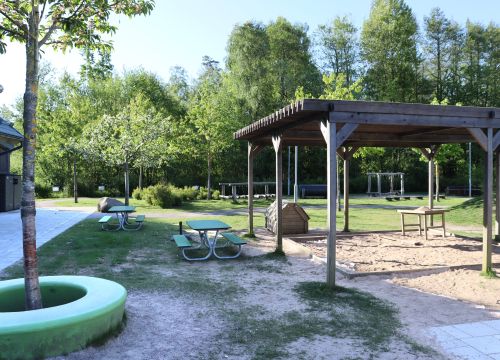 Sandlåda med solskydd – gräsplan och träd i bakgrunden