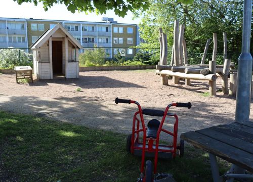 Trehjuling i förgrunden, lekstuga och balansbana i bakgrunden