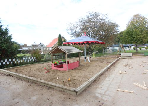 Sandlåda med solskydd och lekstuga, alfabetsbilder på staket i bakgrunden
