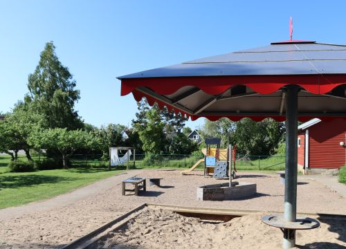 Sandlåda med solskydd – gräsplan, träd och buskar i bakgrunden