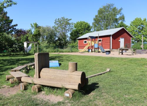 Trätåg på gräsmatta med klätterställning och röd byggnad i bakgrunden