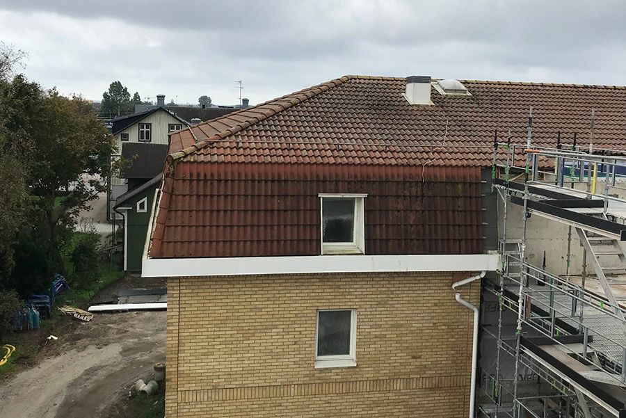 En gul tegelfastighet med byggställningar i förgrunden. Taket är gammalt och slitet.