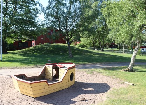 Gul träbåt med grön kulle och träd i bakgrunden