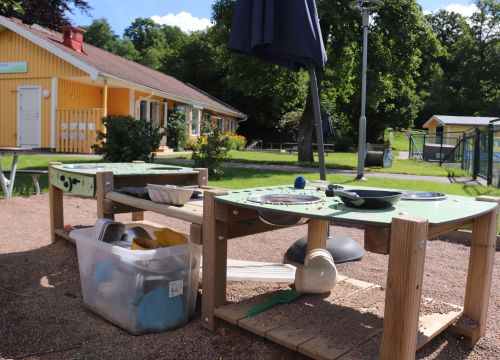 Sandlåda med klätterställning och rutschkana, gräsplan i förgrunden