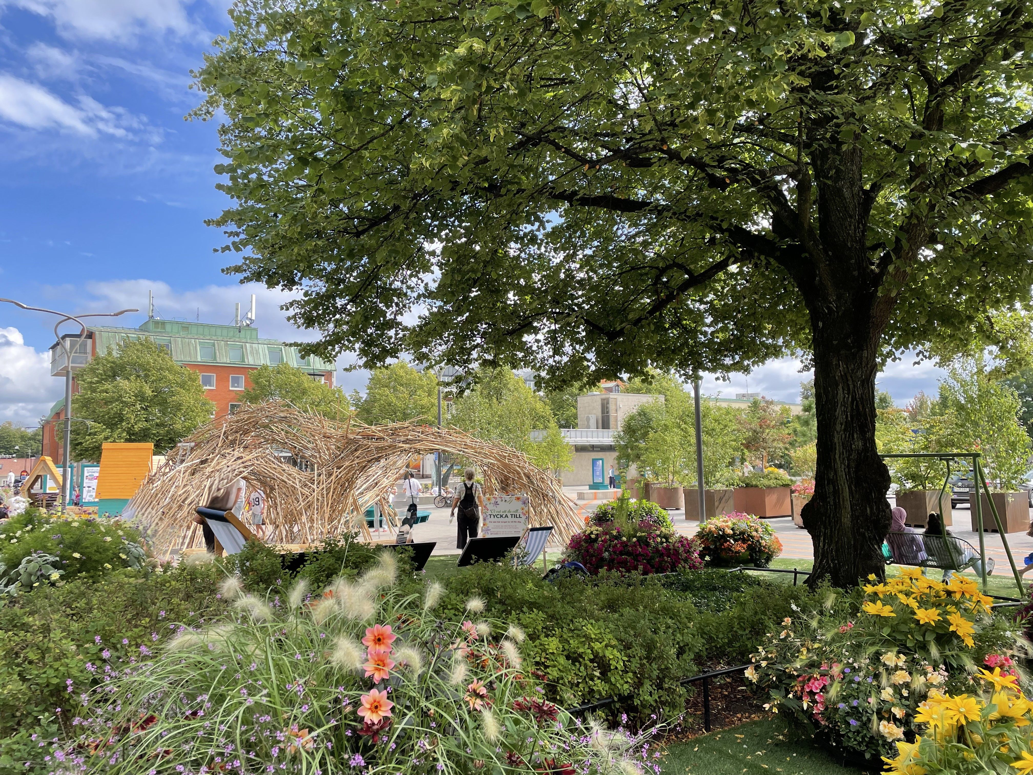 Stortorget i Falkenberg, blå himmel, vy över amfiteater med blomsterlådor och parkering i bakgrunden.