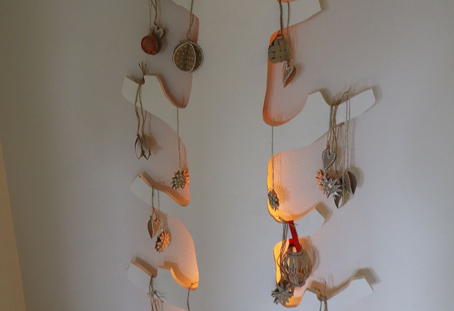 Prydnader i trä hänger på ett platt, vägghängt träd med belysning bakom.