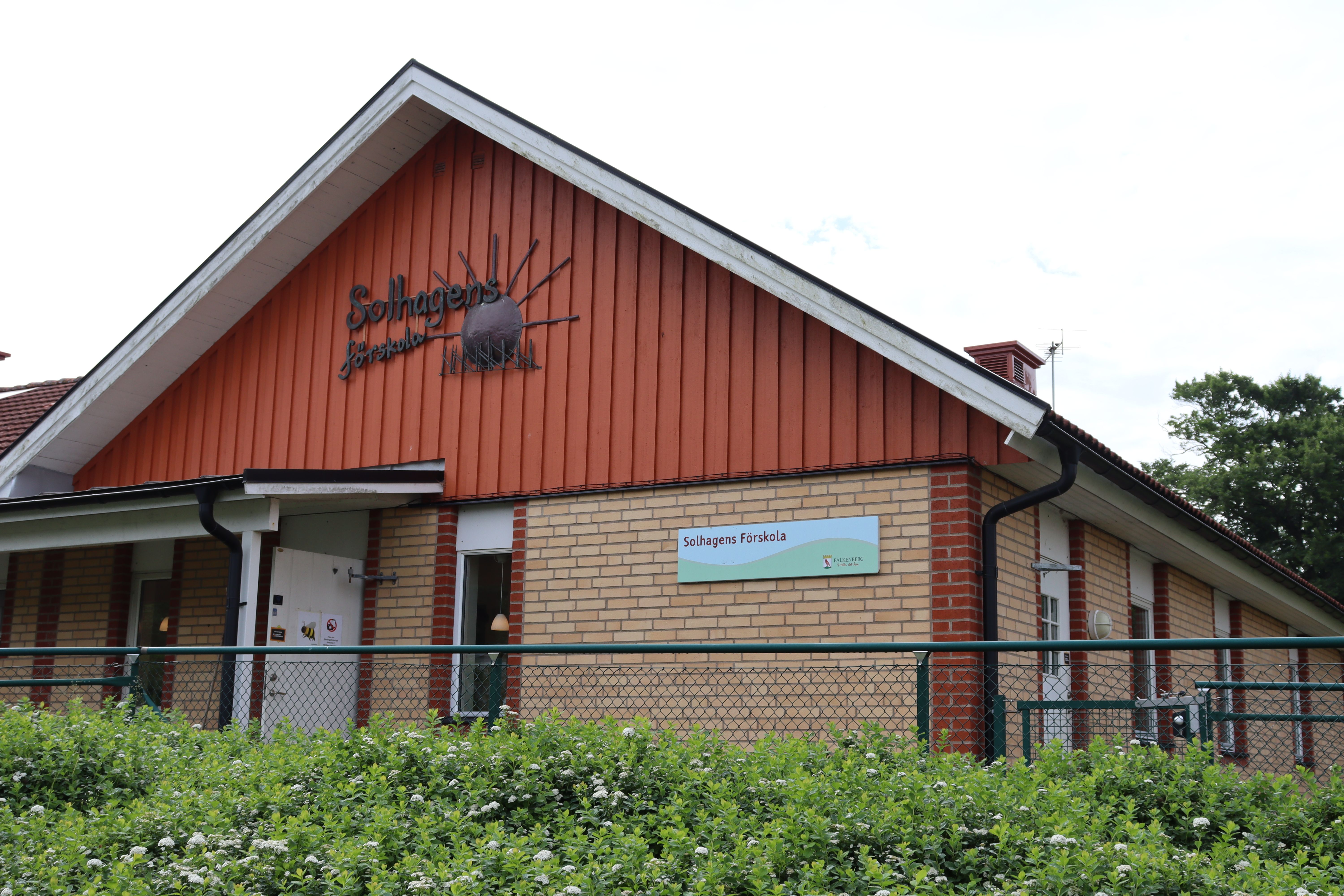 Gul tegelbyggnad med röd träpanel, skylt med Solhagens förskola på gaveln
